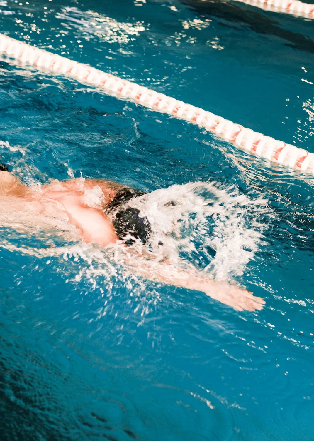 Nadador en estilo libre en la piscina, con salpicaduras intensas y cuerda de carril al fondo.